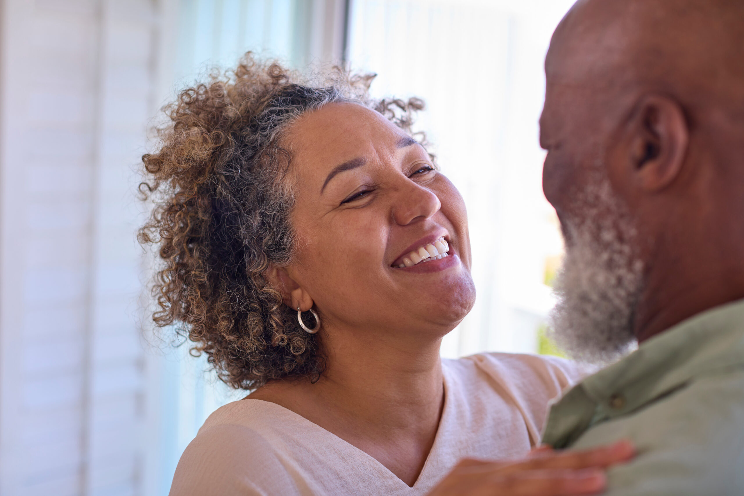 Close Up Of Loving Mature Couple Hugging In Beachfront House Overlooking Ocean For Summer Vacation